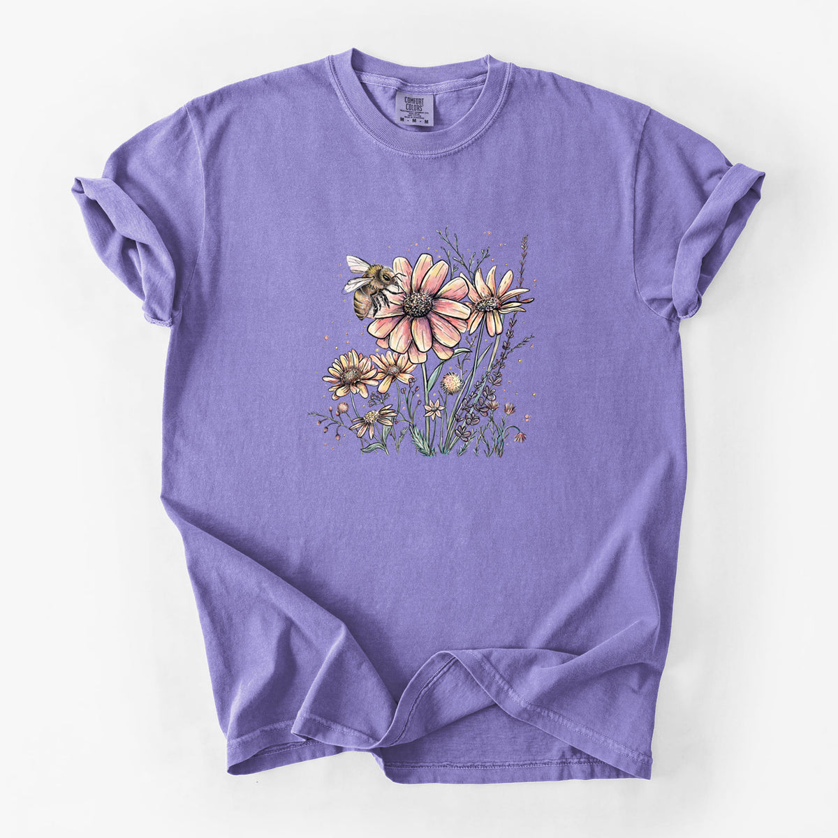 Violet purple Comfort Colors t-shirt laid flat, printed with a soft full-color illustration of a bee flying over pink and purple wildflowers.