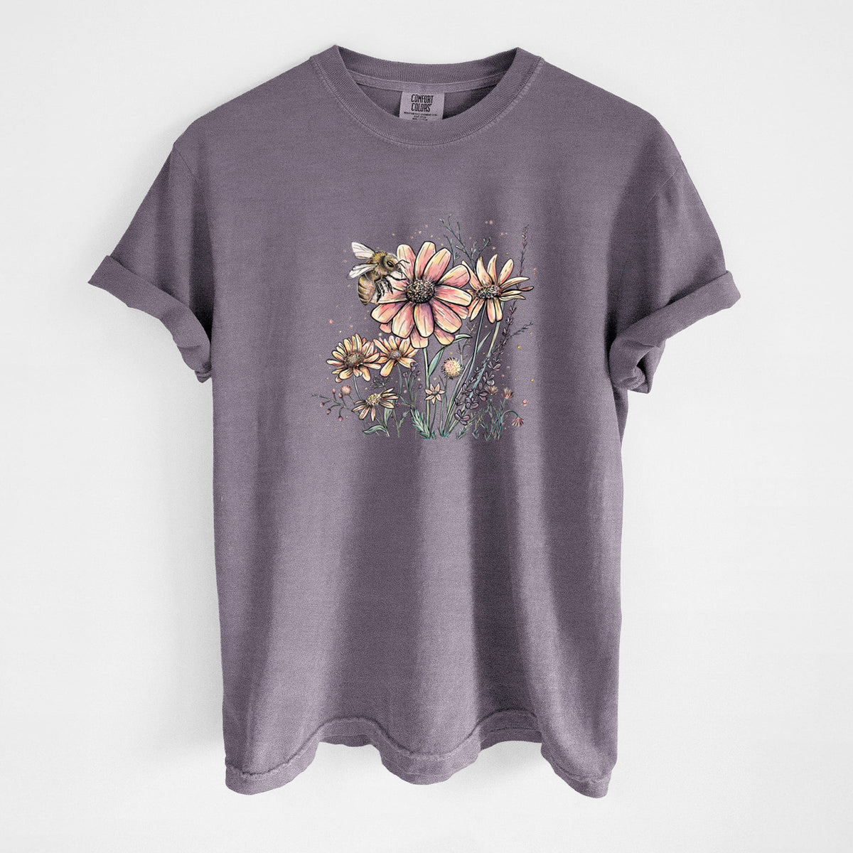 Wine red Comfort Colors t-shirt laid flat, printed with a soft full-color illustration of a bee flying over pink and purple wildflowers.