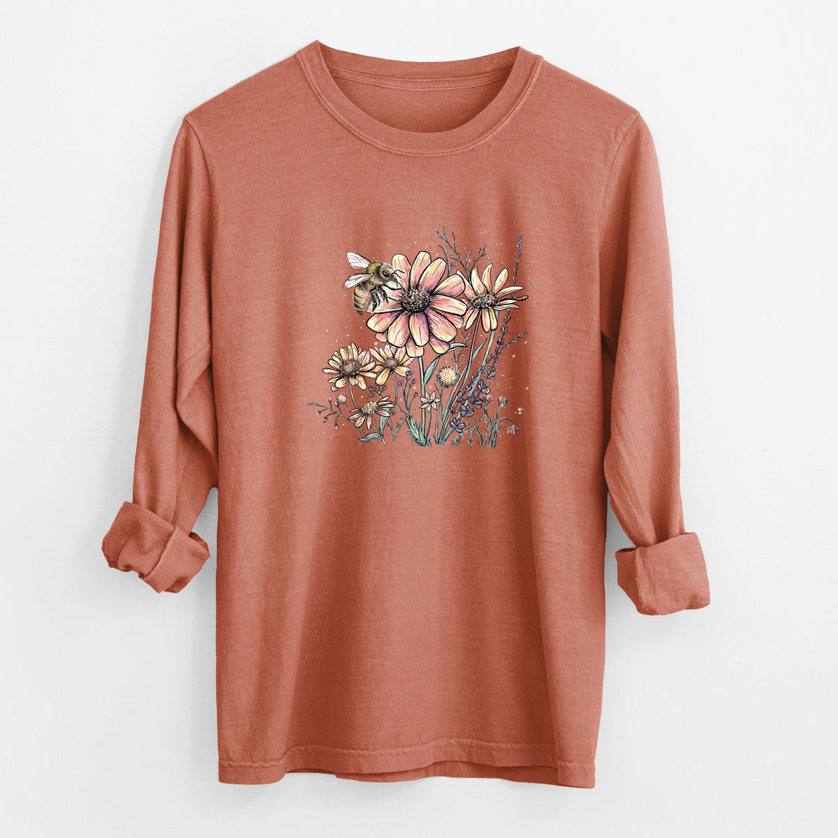 Yam burnt orange Comfort Colors long sleeve shirt laid flat with the cuffs rolled, printed with a soft full-color illustration of a bee flying over pink and purple wildflowers.