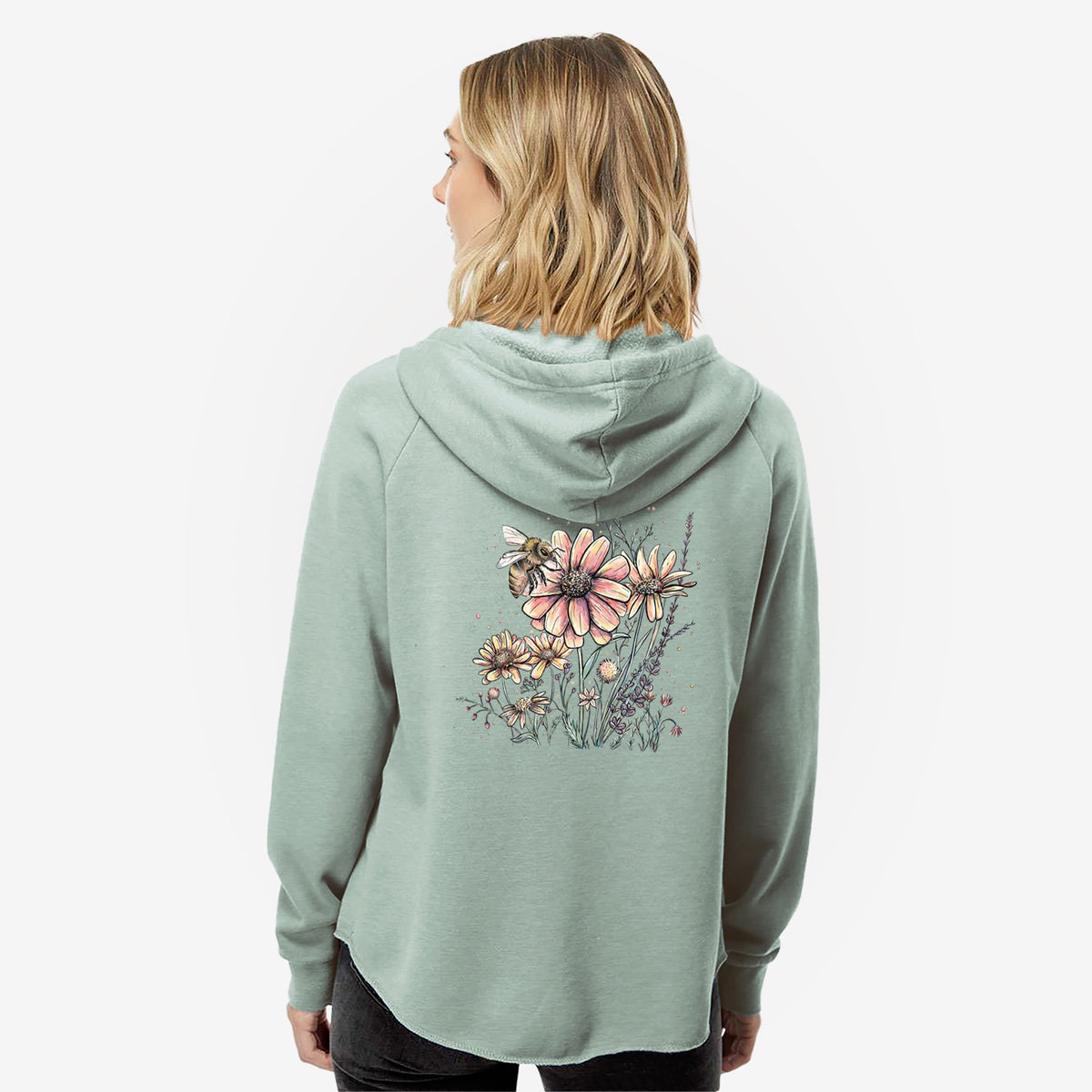 Woman wearing a sage green women's Cali Wave zip-up sweatshirt printed with a soft full-color illustration of a bee flying over pink and purple wildflowers, seen from behind.