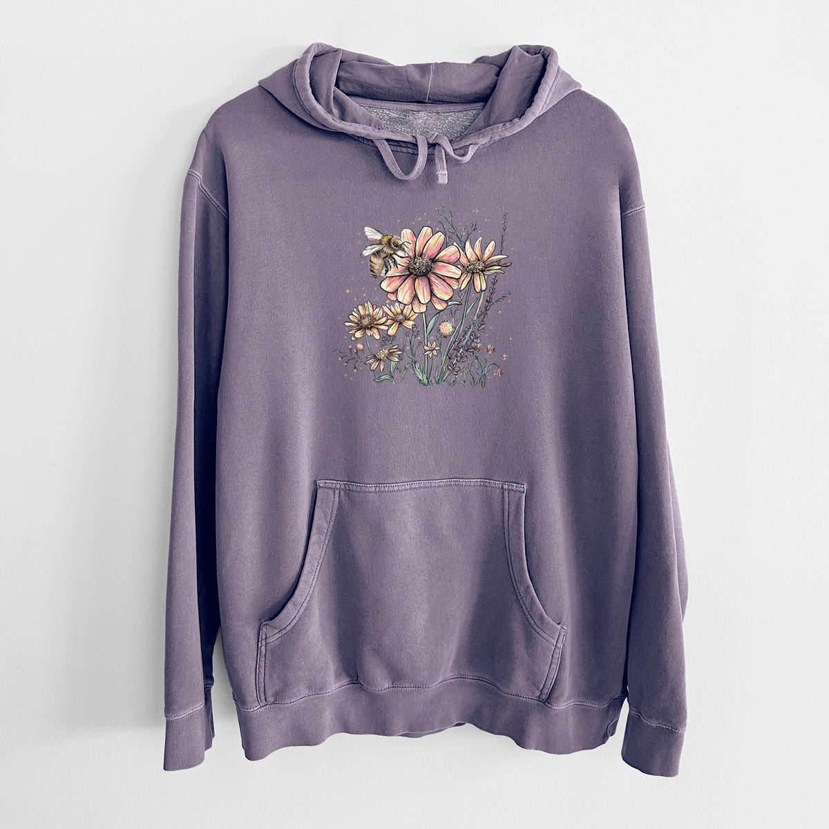 Plum purple pigment dyed hoodie laid flat, printed with a soft full-color illustration of a bee flying over pink and purple wildflowers.