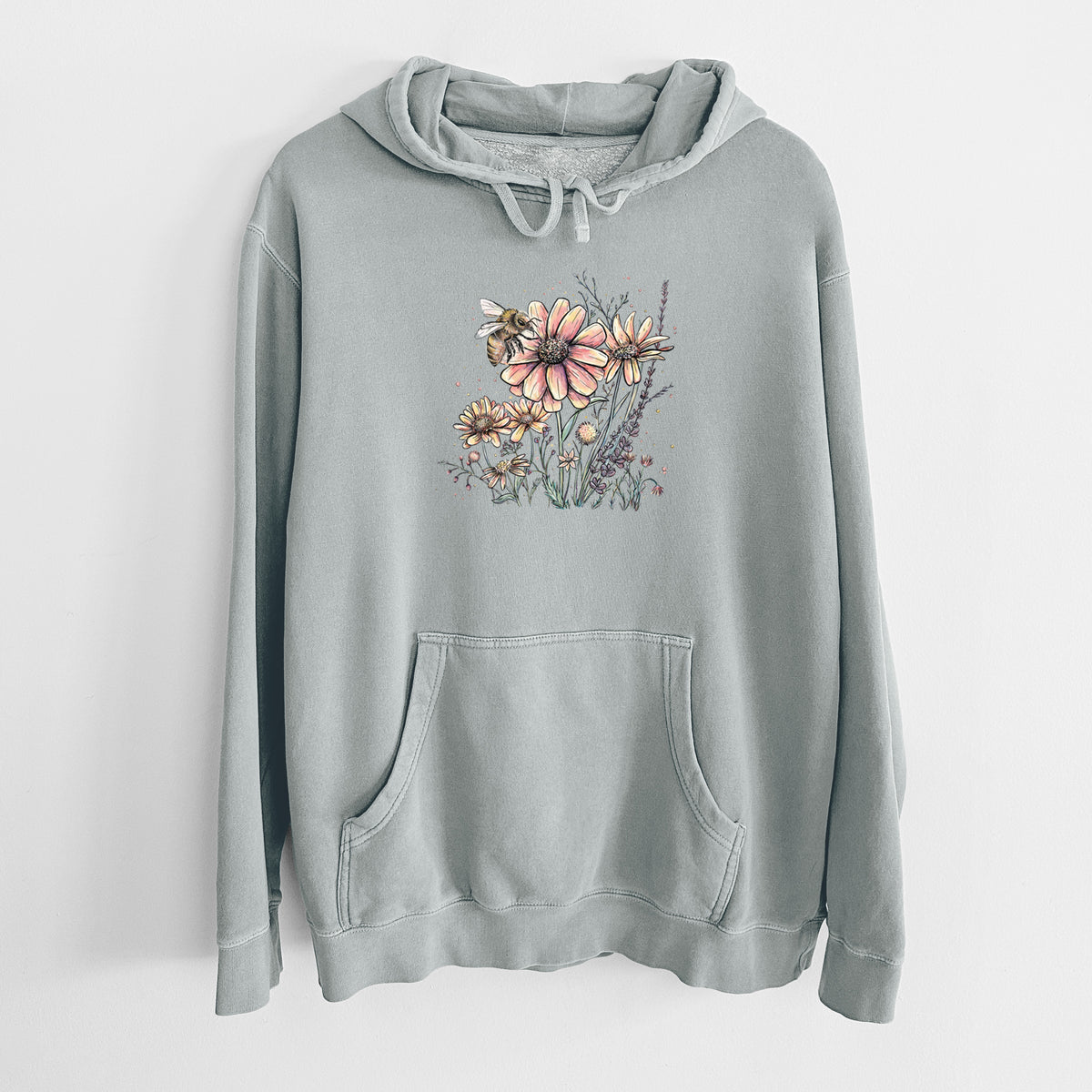Sage green pigment dyed hoodie laid flat, printed with a soft full-color illustration of a bee flying over pink and purple wildflowers.