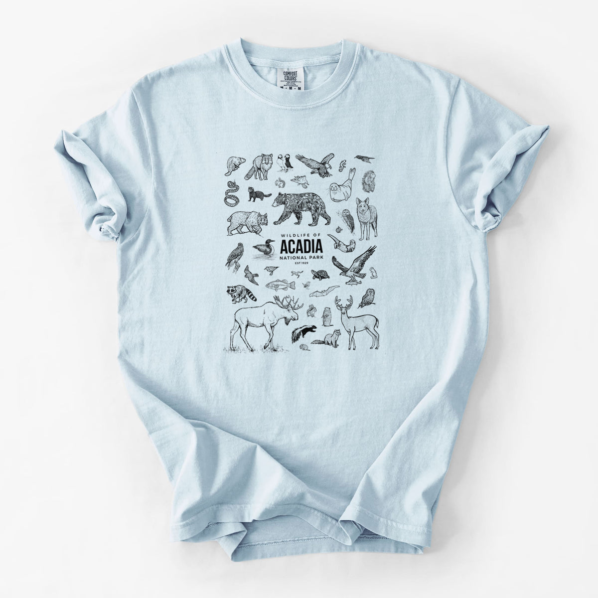 Chambray blue Comfort Colors t-shirt laid flat, printed with a collection of black ink wildlife illustrations surrounding the words Acadia National Park.
