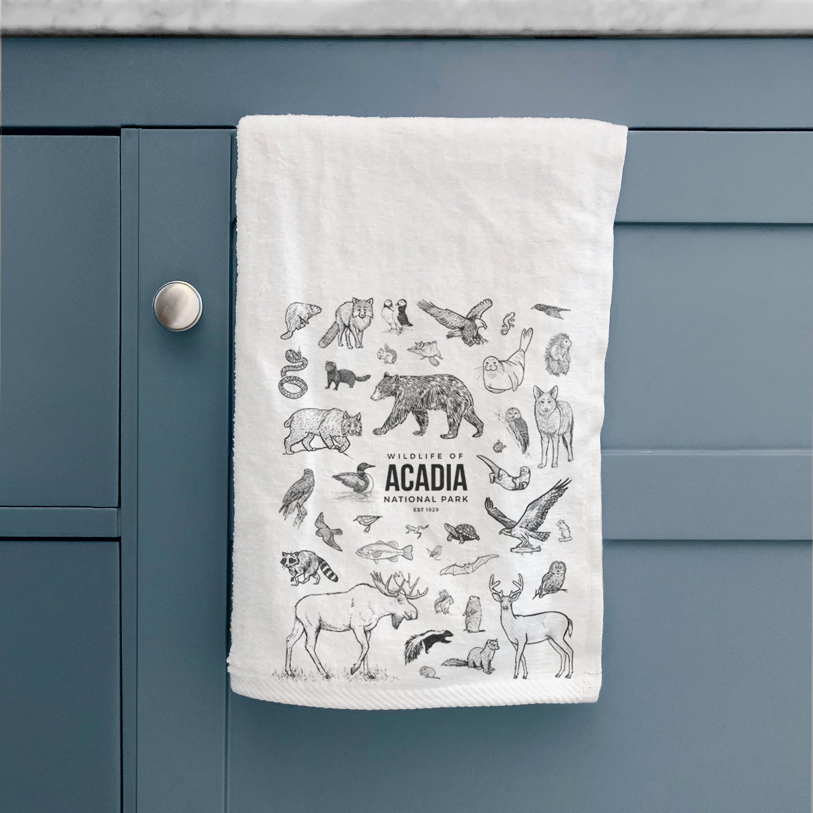 White hand towel printed with a collection of black ink wildlife illustrations surrounding the words Acadia National Park.