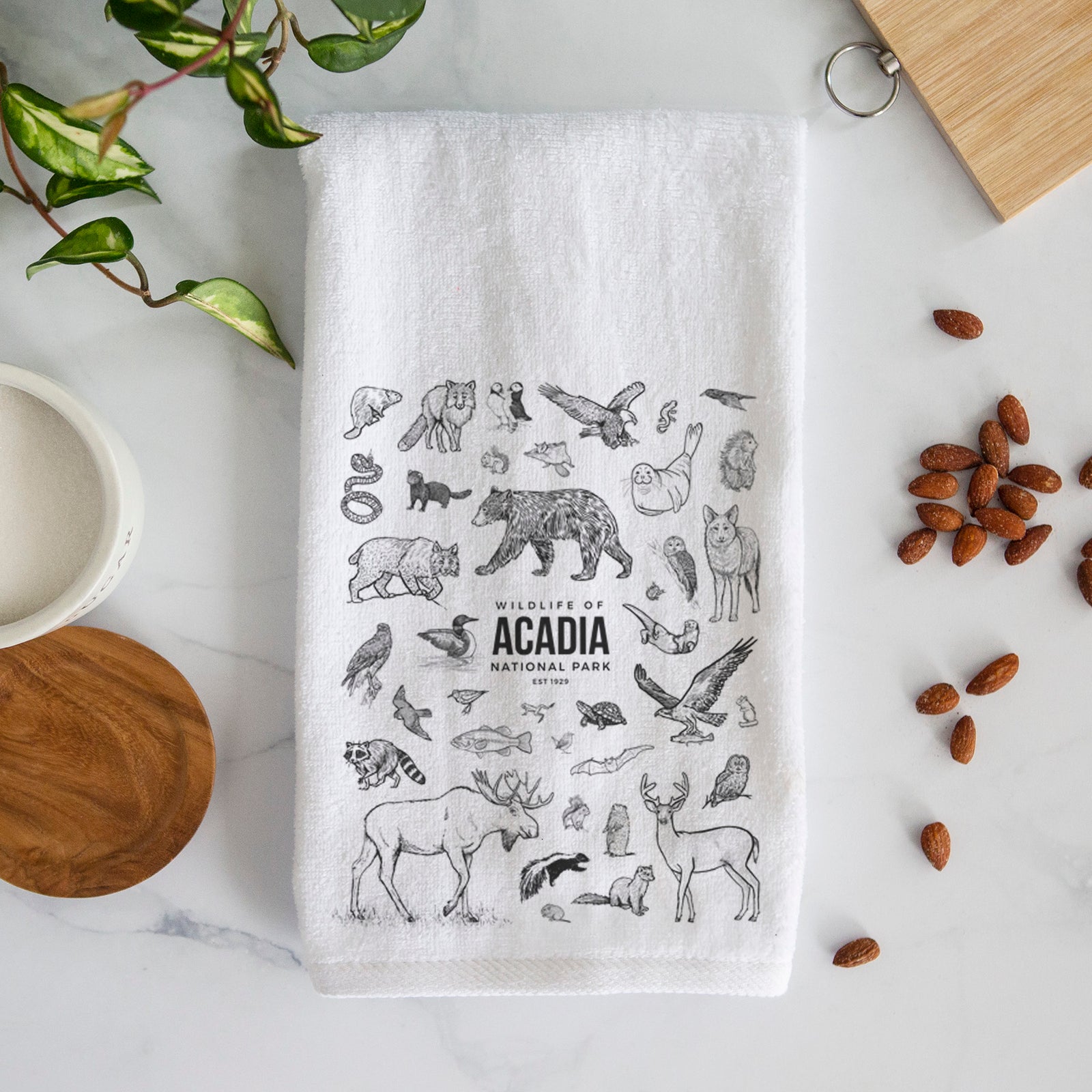 White hand towel printed with a collection of black ink wildlife illustrations surrounding the words Acadia National Park.