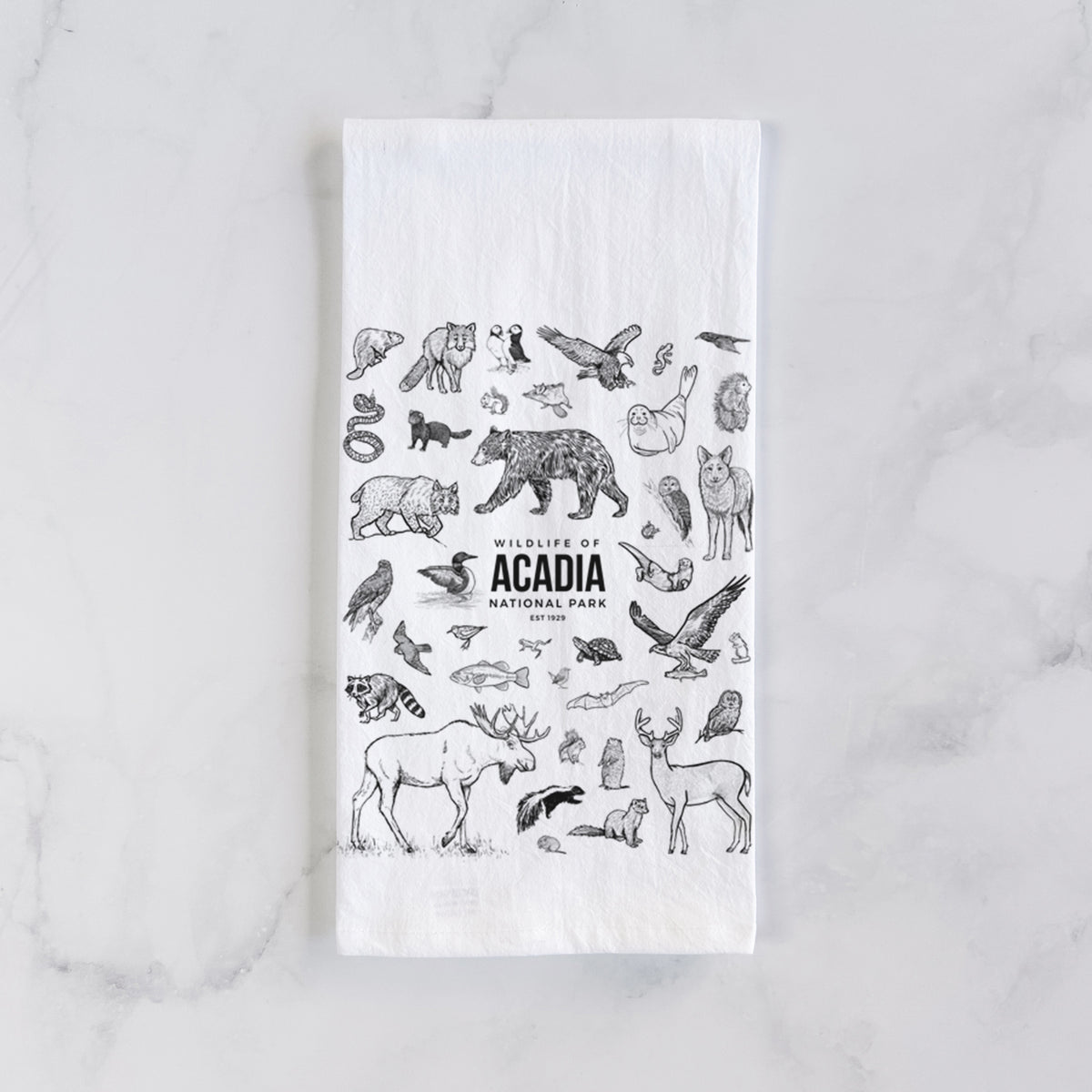 White cotton tea towel laid flat on marble, printed with a collection of black ink wildlife illustrations surrounding the words Acadia National Park.