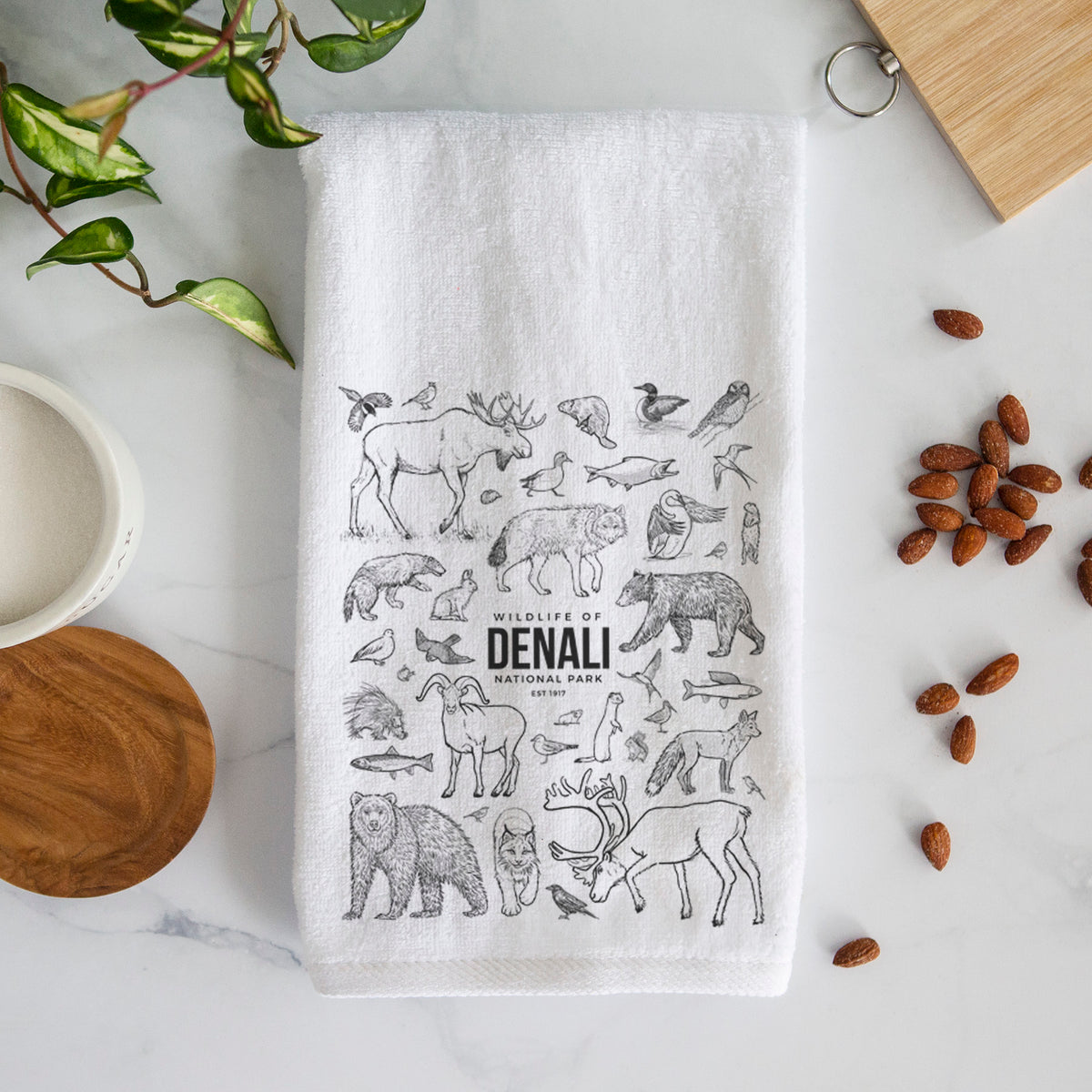White hand towel printed with a collection of black ink wildlife illustrations surrounding the words Denali National Park.