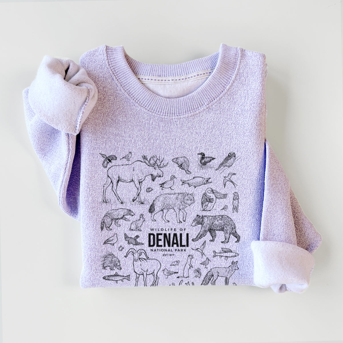 Ice purple knit sweatshirt printed with a collection of black ink wildlife illustrations surrounding the words Denali National Park, styled flat.