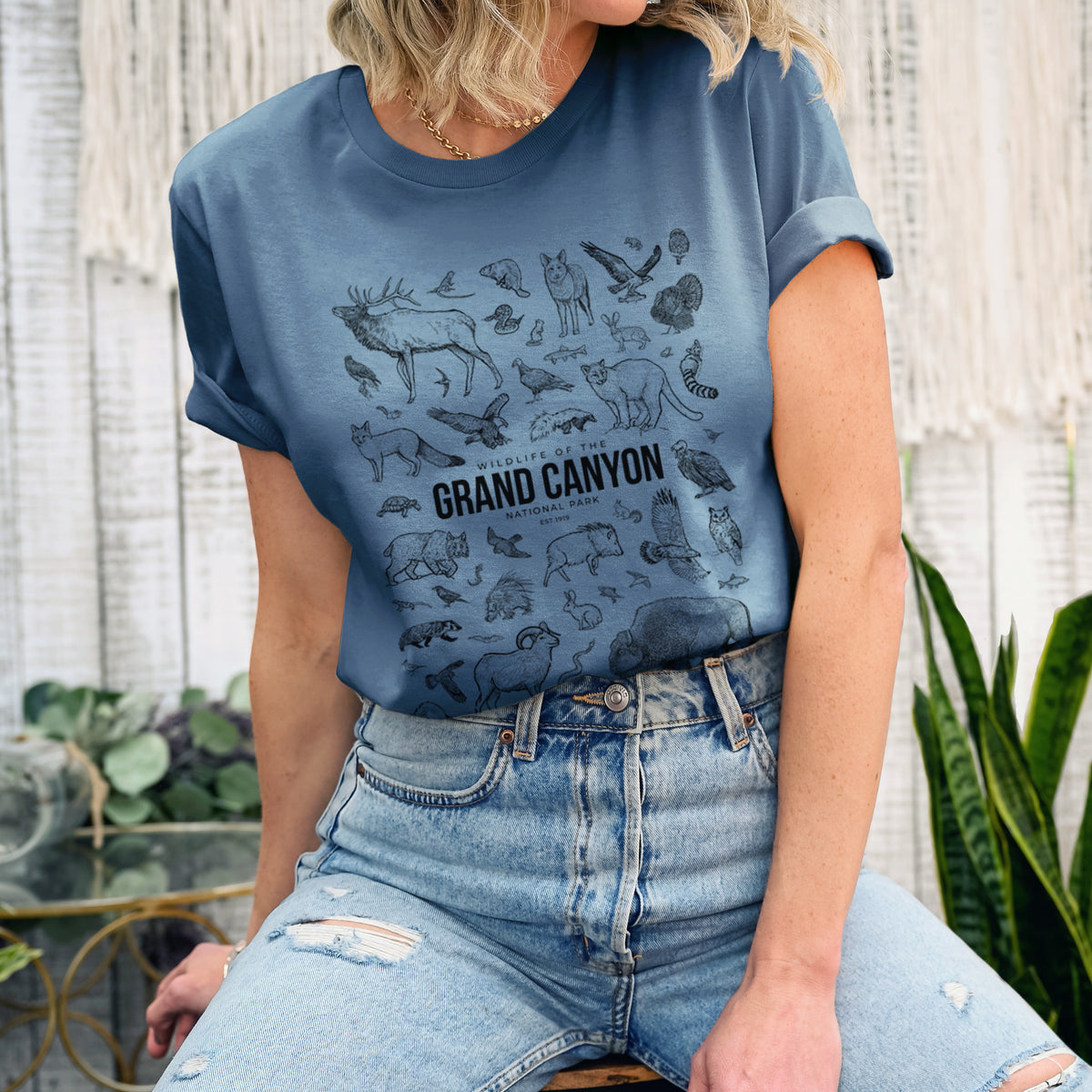 Woman wearing a steel blue lightweight cotton t-shirt printed with a collection of black ink wildlife illustrations surrounding the words Grand Canyon National Park.