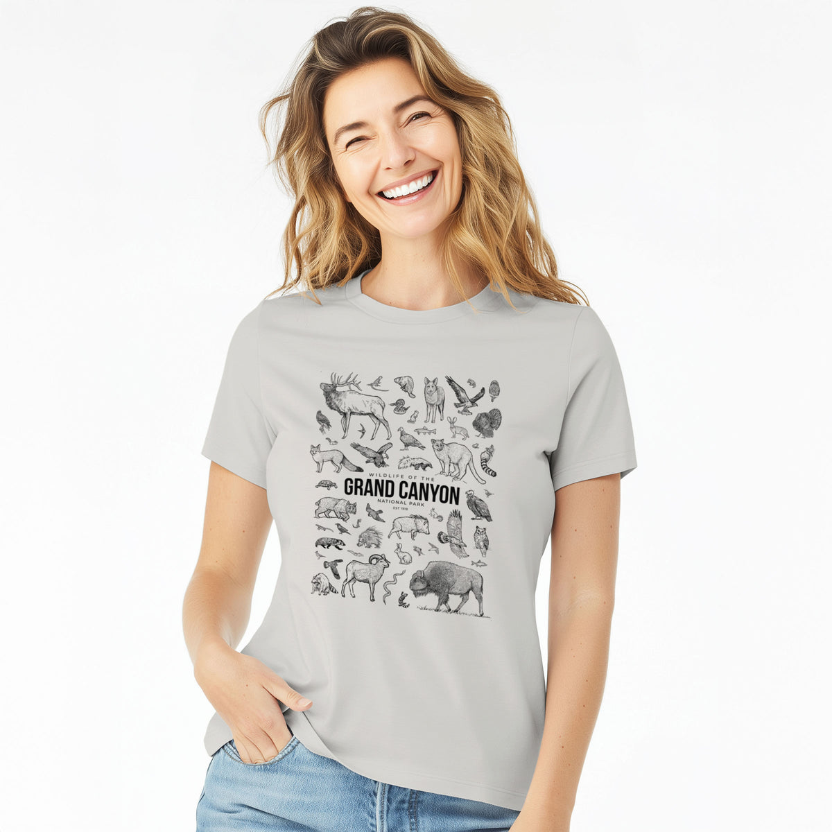 Woman wearing a lunar grey women's relaxed fit cotton t-shirt printed with a collection of black ink wildlife illustrations surrounding the words Grand Canyon National Park.
