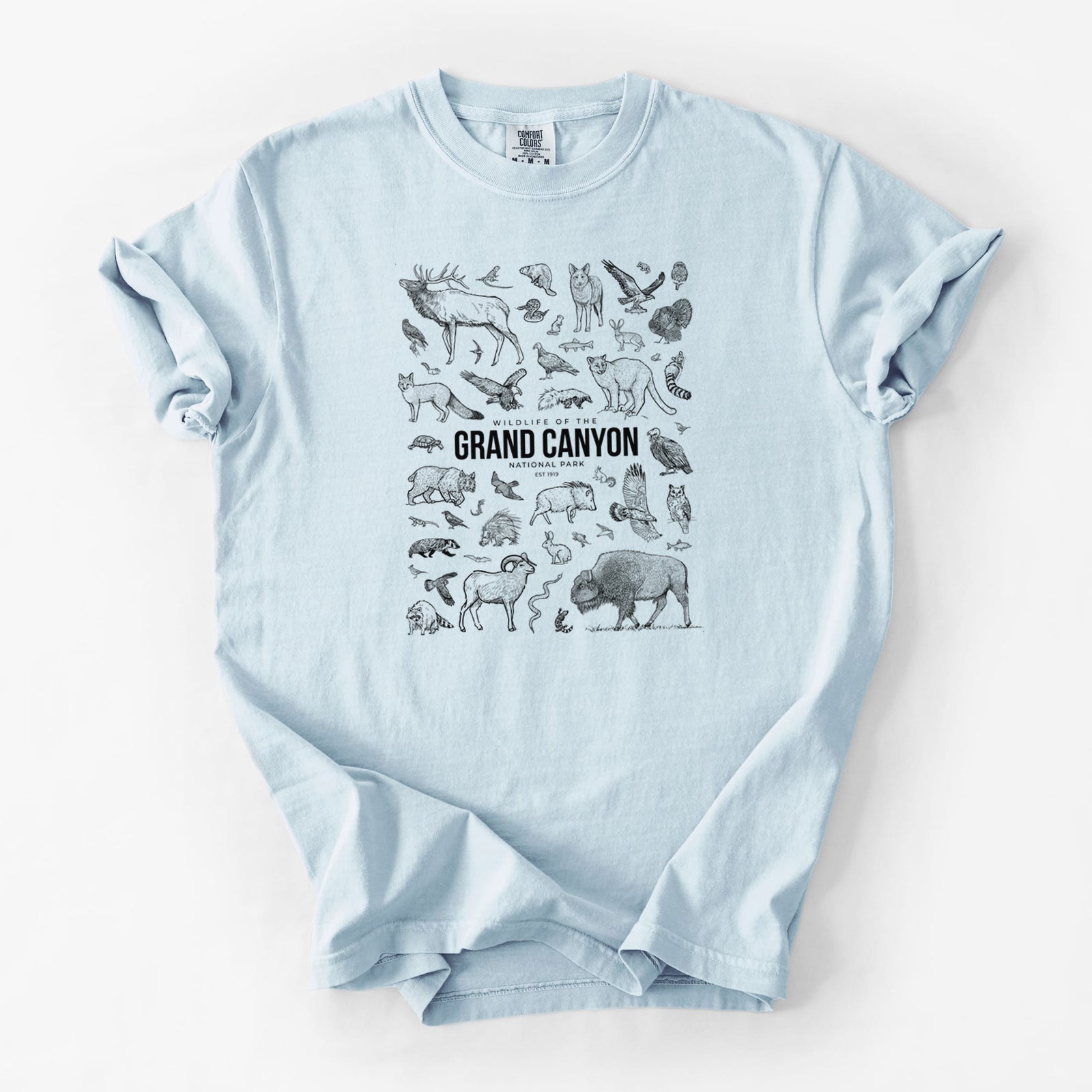 Blue jean Comfort Colors t-shirt laid flat, printed with a collection of black ink wildlife illustrations surrounding the words Grand Canyon National Park.