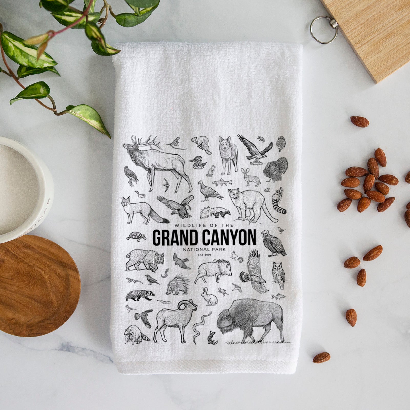 White hand towel printed with a collection of black ink wildlife illustrations surrounding the words Grand Canyon National Park.