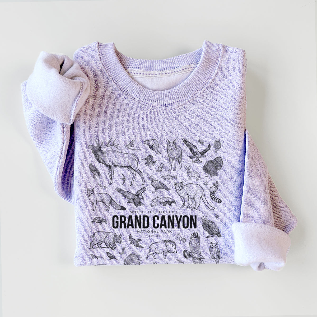Ice purple knit sweatshirt printed with a collection of black ink wildlife illustrations surrounding the words Grand Canyon National Park, styled flat.