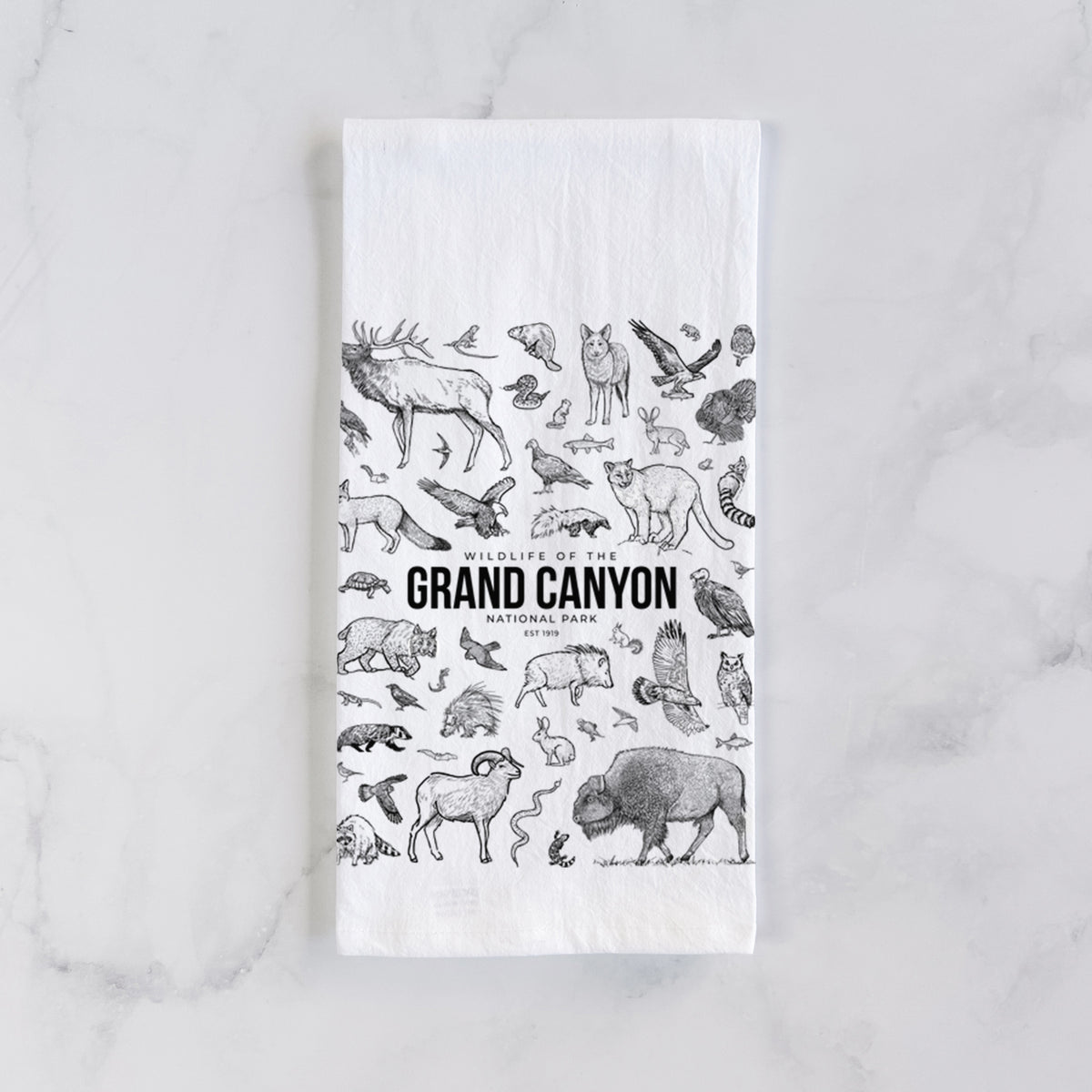 White cotton tea towel laid flat on marble, printed with a collection of black ink wildlife illustrations surrounding the words Grand Canyon National Park.
