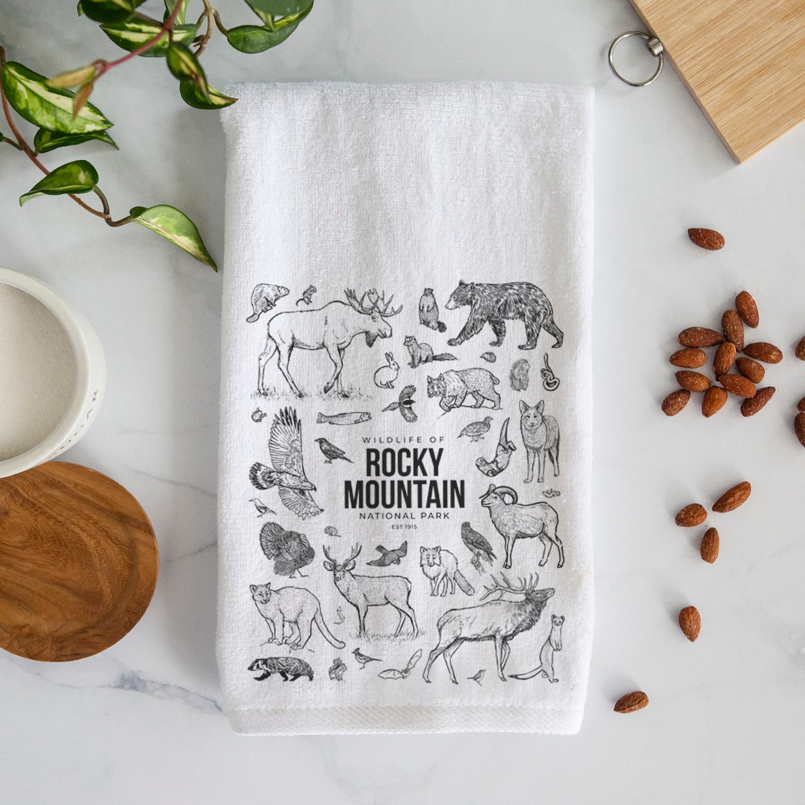 White hand towel printed with a collection of black ink wildlife illustrations surrounding the words Rocky Mountain National Park.