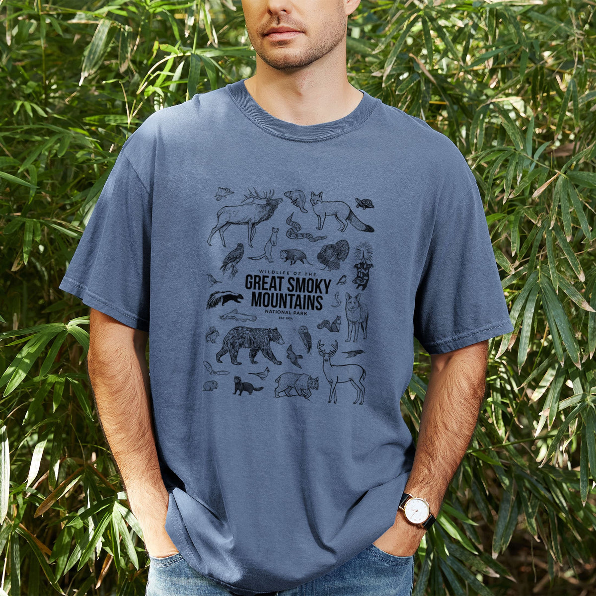 Man wearing a Comfort Colors t-shirt printed with a collection of black ink wildlife illustrations surrounding the words Great Smoky Mountains National Park, outdoors.