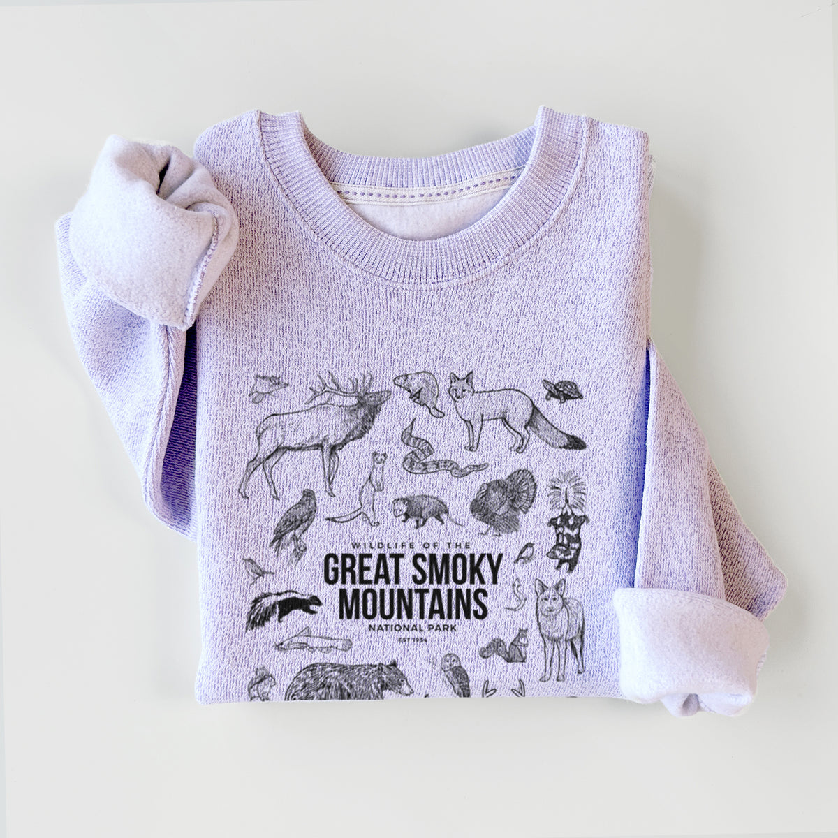 Ice purple knit sweatshirt printed with a collection of black ink wildlife illustrations surrounding the words Great Smoky Mountains National Park, styled flat.
