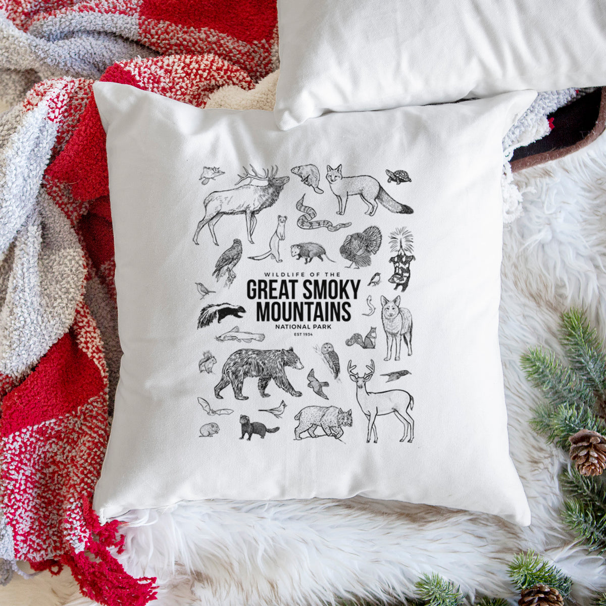 White pillow cover printed with a collection of black ink wildlife illustrations surrounding the words Great Smoky Mountains National Park, on a woven chair.