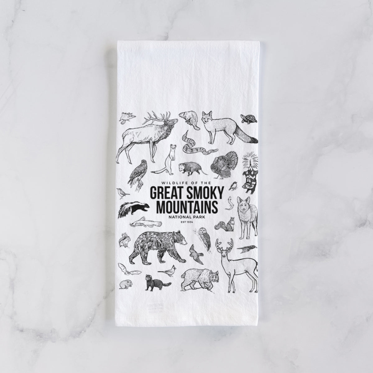 White cotton tea towel laid flat on marble, printed with a collection of black ink wildlife illustrations surrounding the words Great Smoky Mountains National Park.