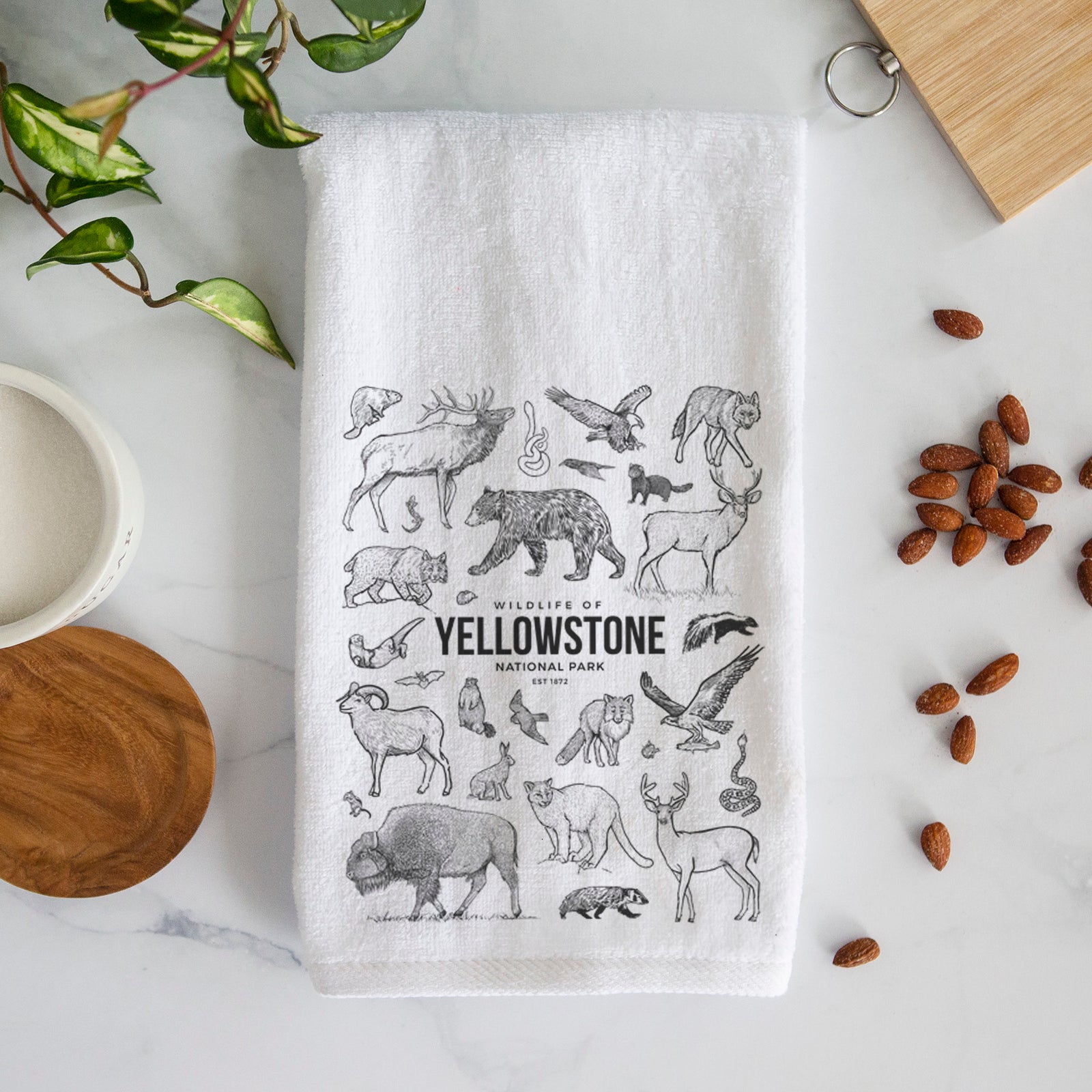 White hand towel printed with a collection of black ink wildlife illustrations surrounding the words Yellowstone National Park.