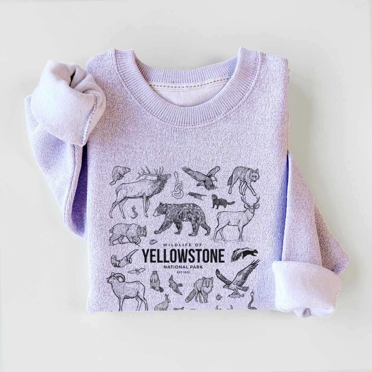 Ice purple knit sweatshirt printed with a collection of black ink wildlife illustrations surrounding the words Yellowstone National Park, styled flat.