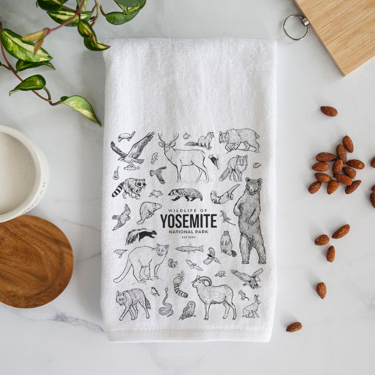 White hand towel printed with a collection of black ink wildlife illustrations surrounding the words Yosemite National Park.