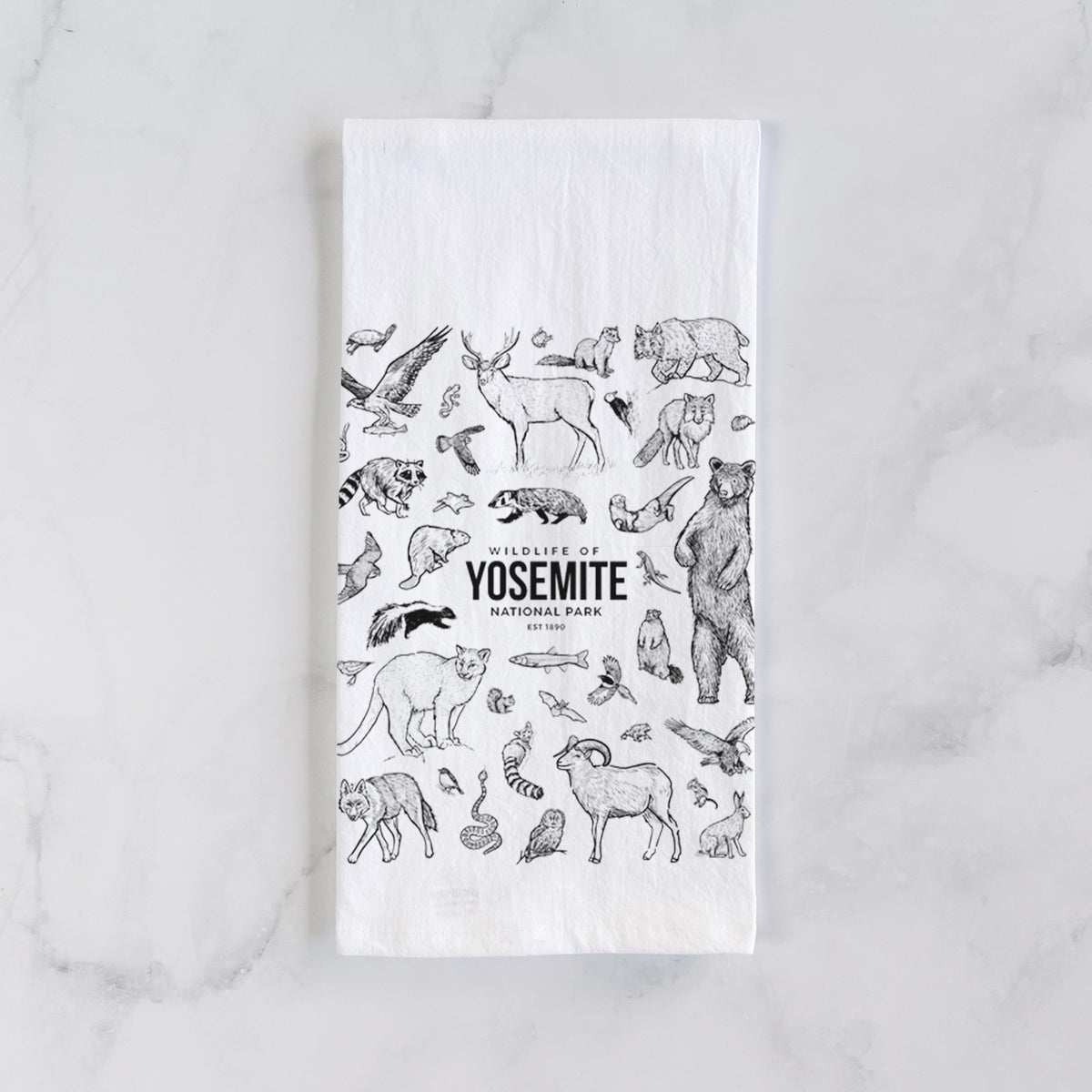 White cotton tea towel laid flat on marble, printed with a collection of black ink wildlife illustrations surrounding the words Yosemite National Park.