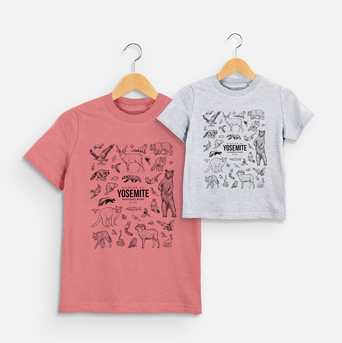 Two youth t-shirts in different colors on hangers, printed with a collection of black ink wildlife illustrations surrounding the words Yosemite National Park.