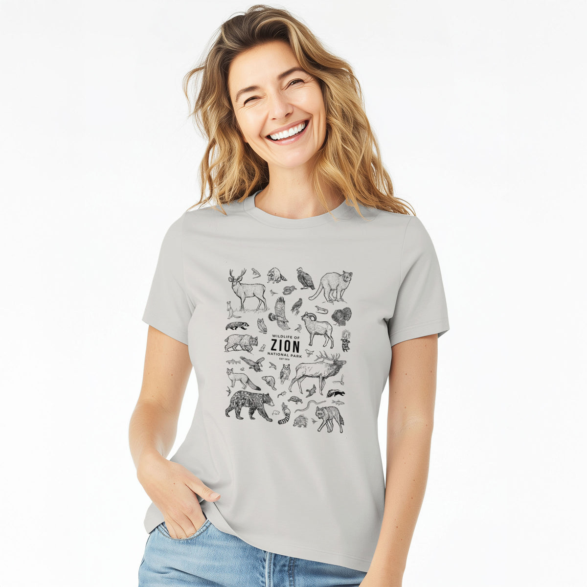 Woman wearing a lunar grey women's relaxed fit cotton t-shirt printed with a collection of black ink wildlife illustrations surrounding the words Zion National Park.