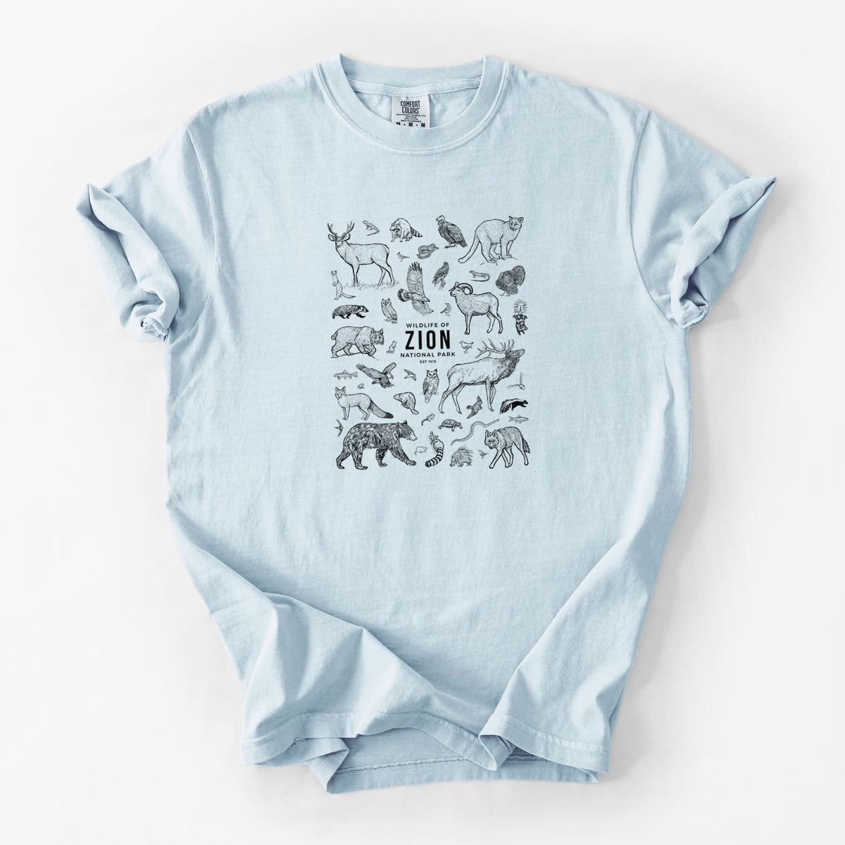 Chambray blue Comfort Colors t-shirt laid flat, printed with a collection of black ink wildlife illustrations surrounding the words Zion National Park.