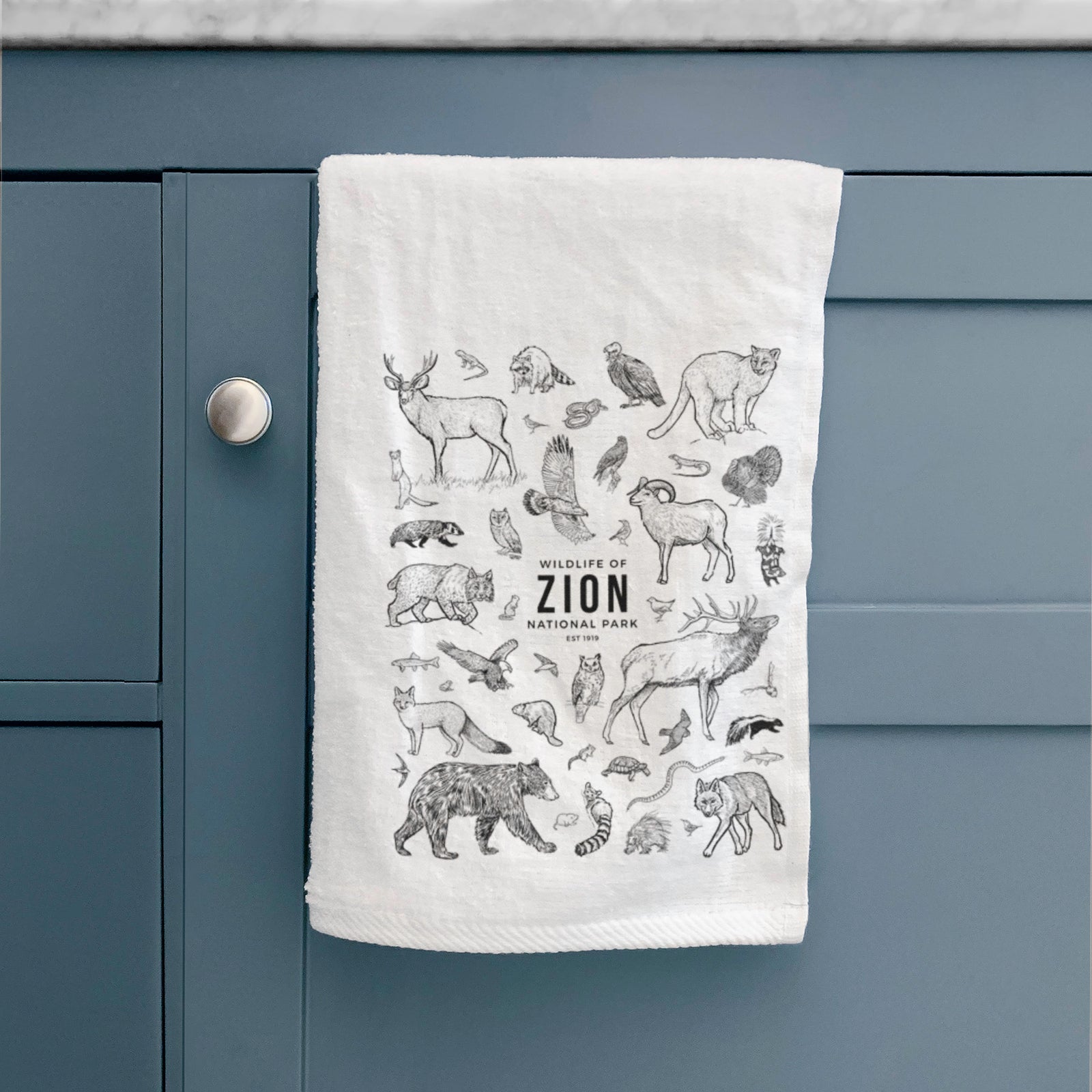 White hand towel printed with a collection of black ink wildlife illustrations surrounding the words Zion National Park.