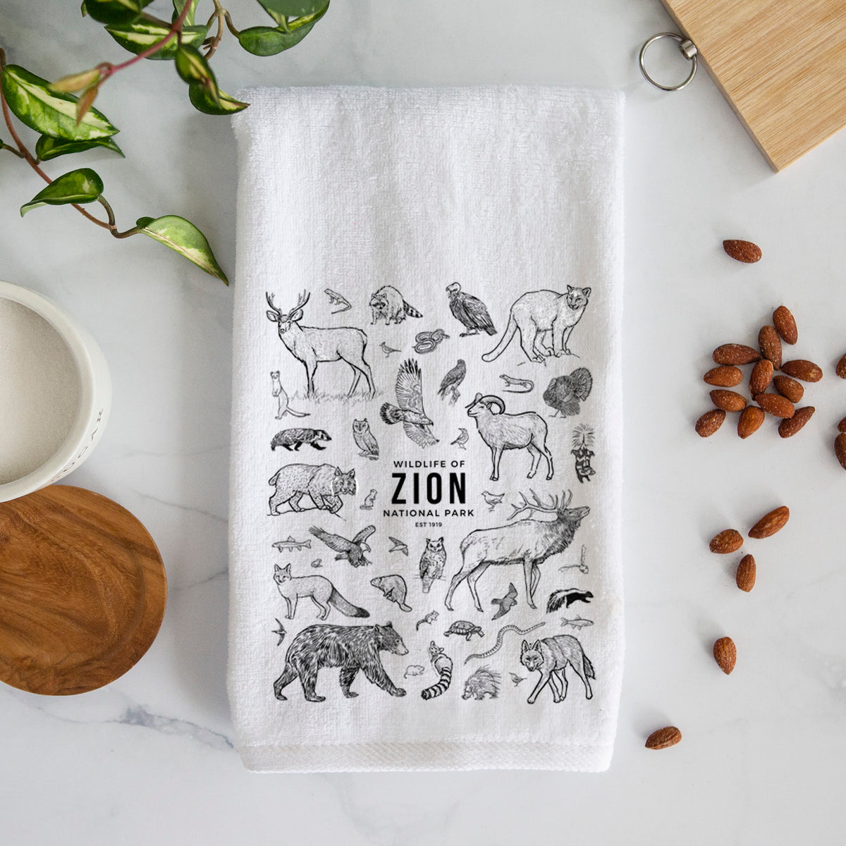 White hand towel printed with a collection of black ink wildlife illustrations surrounding the words Zion National Park.