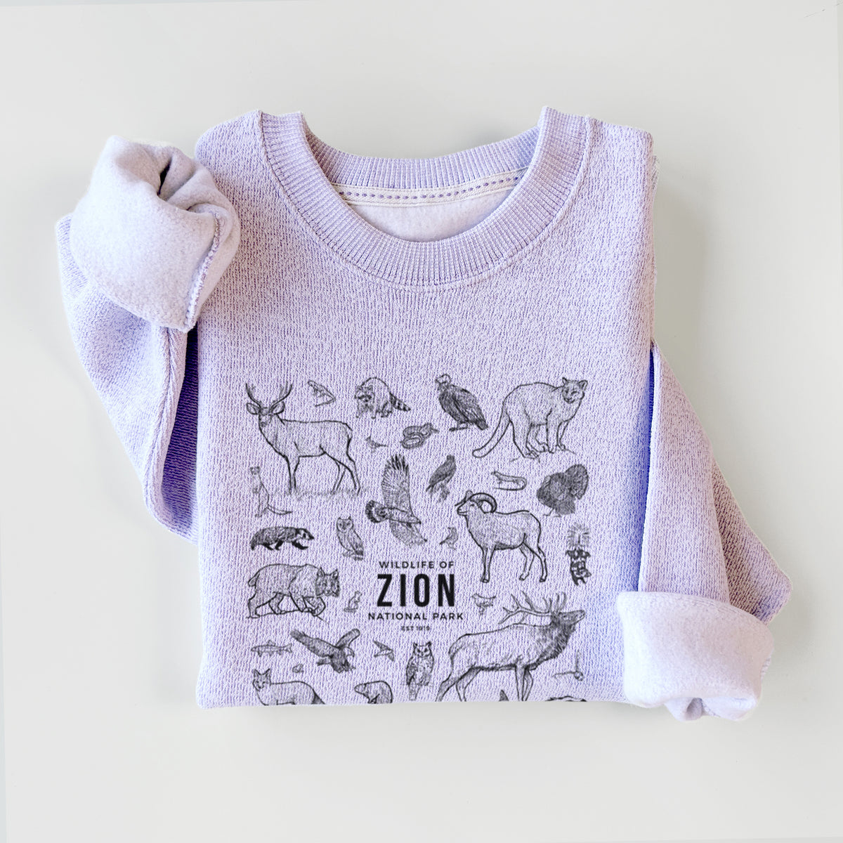 Ice purple knit sweatshirt printed with a collection of black ink wildlife illustrations surrounding the words Zion National Park, styled flat.