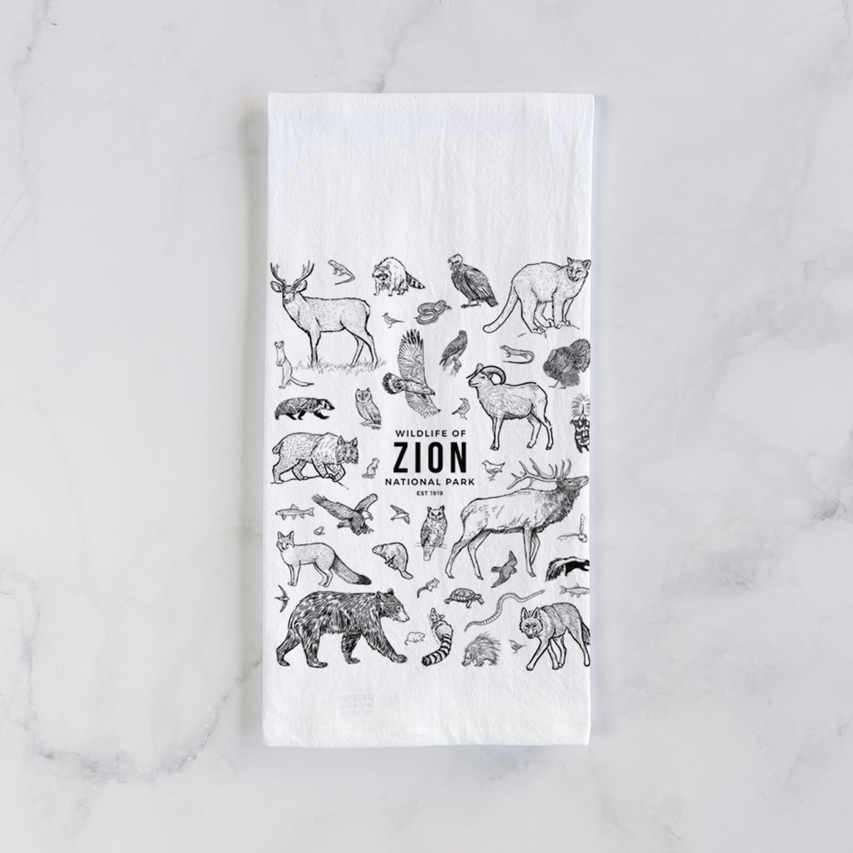 White cotton tea towel laid flat on marble, printed with a collection of black ink wildlife illustrations surrounding the words Zion National Park.