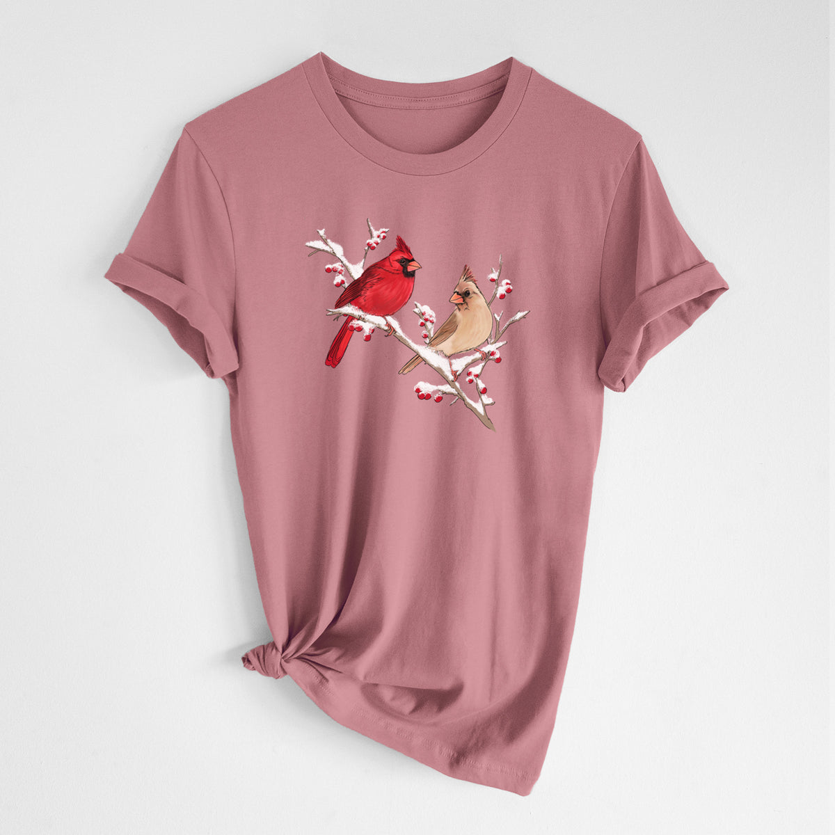 Mauve pink lightweight cotton t-shirt laid flat with the sleeves rolled, printed with a full-color illustration of a male and female northern cardinal perched on a snowy branch with red berries.