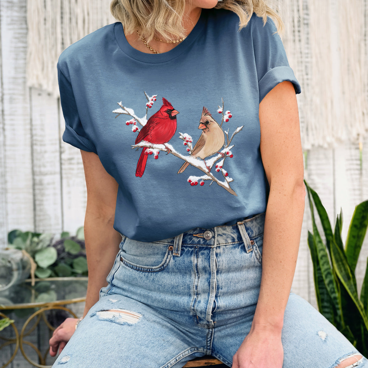 Woman wearing a steel blue lightweight cotton t-shirt printed with a full-color illustration of a male and female northern cardinal perched on a snowy branch with red berries.