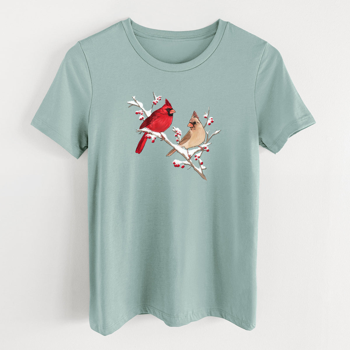 Dusty blue women's relaxed fit cotton t-shirt laid flat, printed with a full-color illustration of a male and female northern cardinal perched on a snowy branch with red berries.