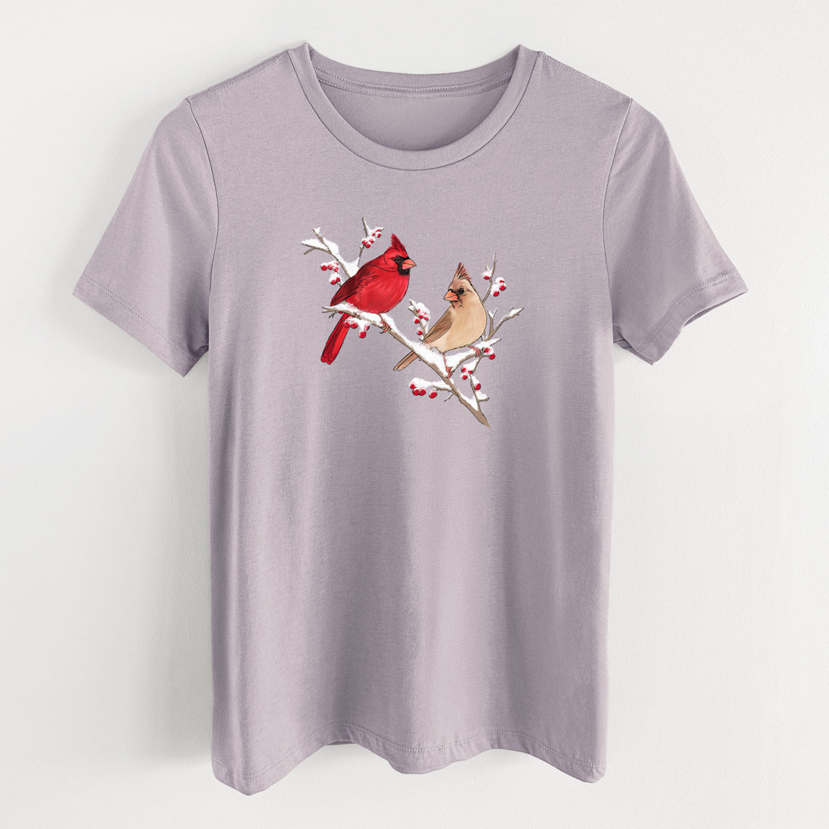 Light violet women's relaxed fit cotton t-shirt laid flat, printed with a full-color illustration of a male and female northern cardinal perched on a snowy branch with red berries.
