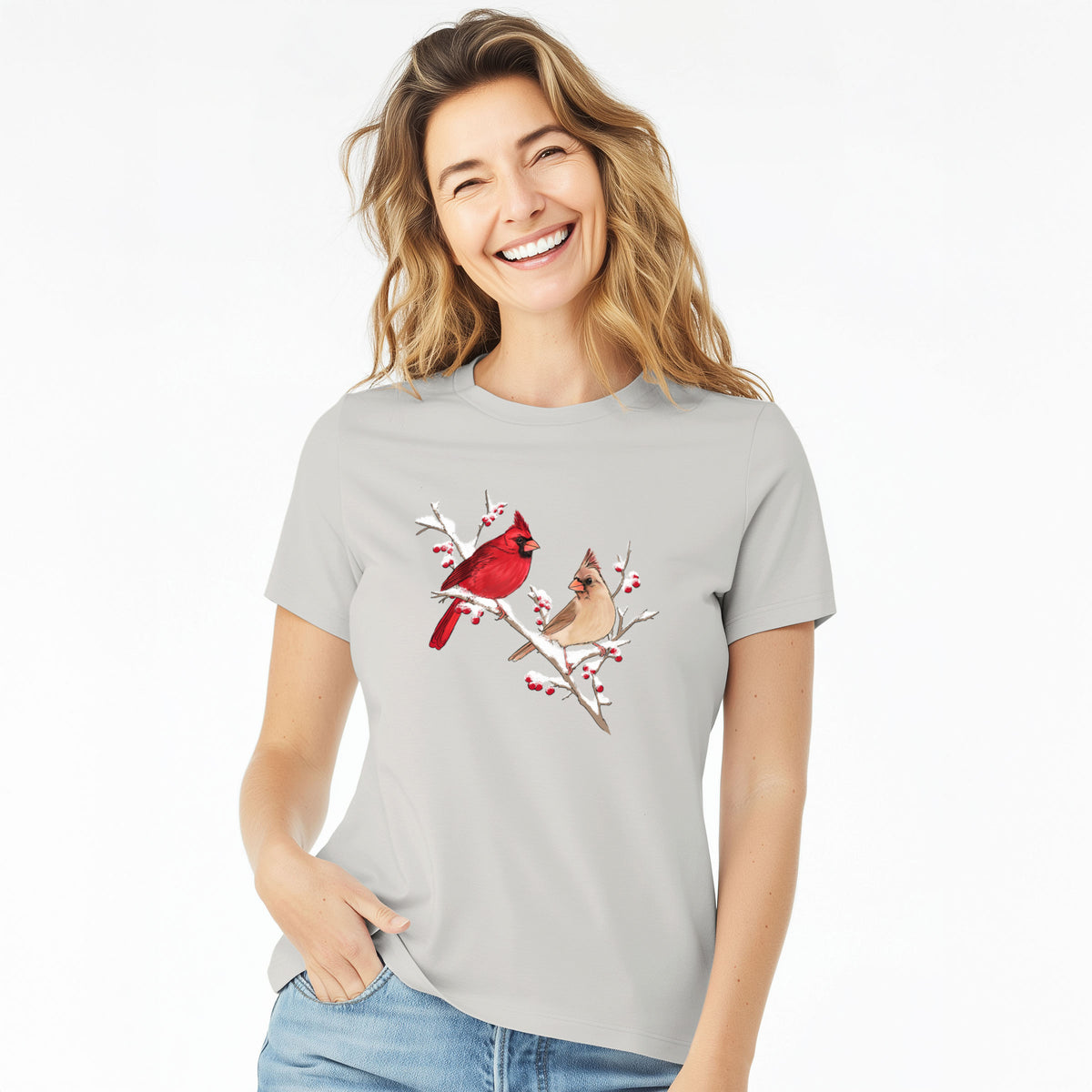 Woman wearing a lunar grey women's relaxed fit cotton t-shirt printed with a full-color illustration of a male and female northern cardinal perched on a snowy branch with red berries.