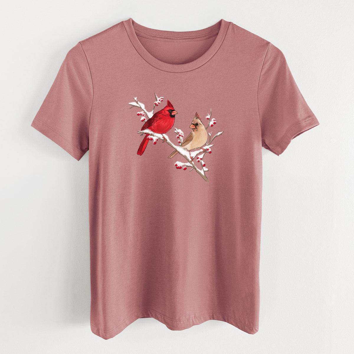 Mauve pink women's relaxed fit cotton t-shirt laid flat, printed with a full-color illustration of a male and female northern cardinal perched on a snowy branch with red berries.