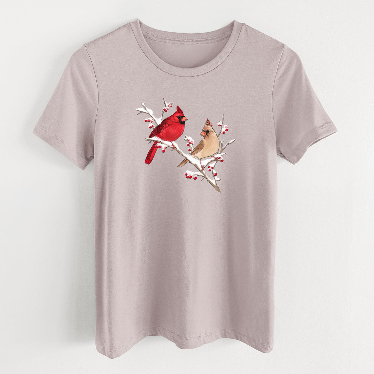 Pink gravel women's relaxed fit cotton t-shirt laid flat, printed with a full-color illustration of a male and female northern cardinal perched on a snowy branch with red berries.