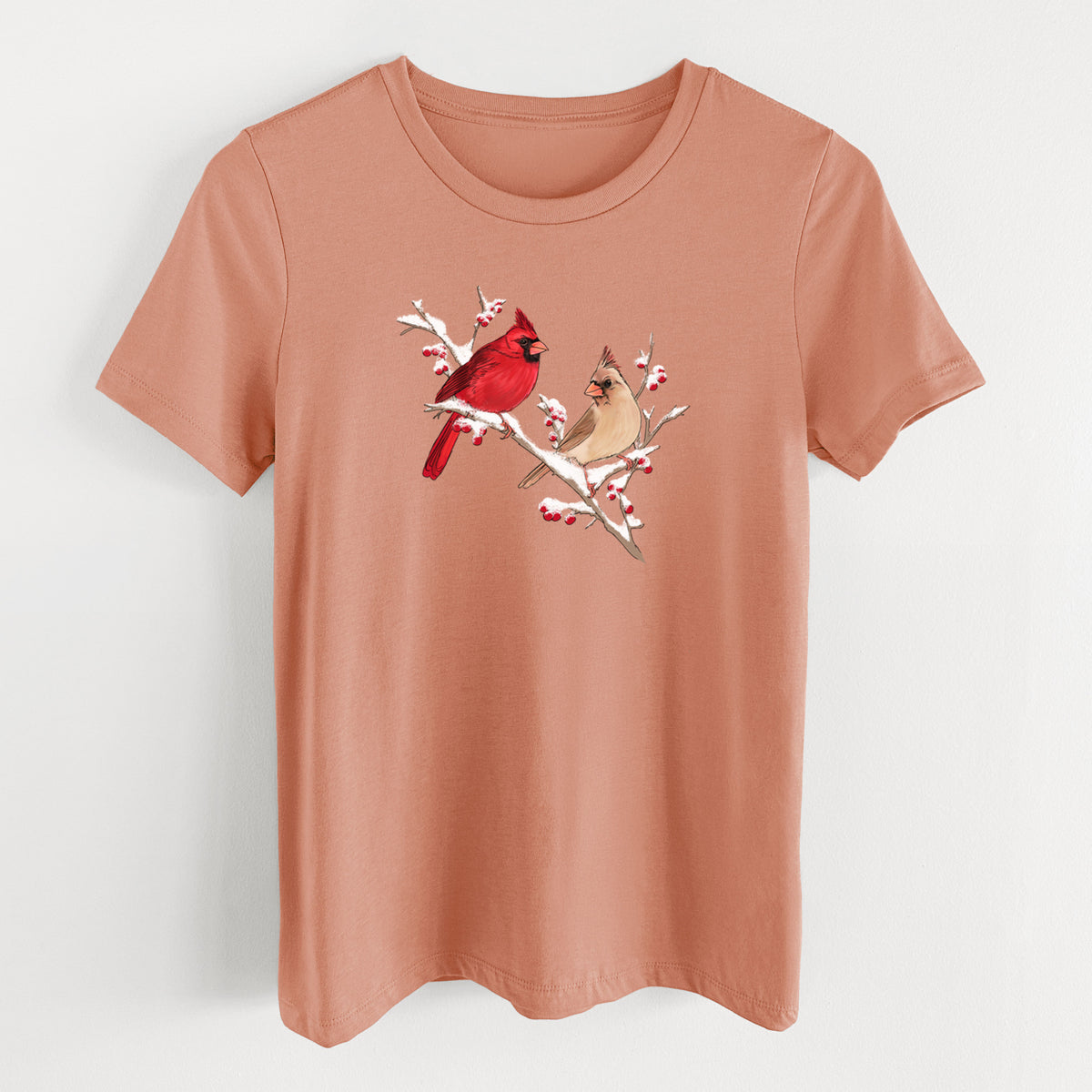 Terracotta orange women's relaxed fit cotton t-shirt laid flat, printed with a full-color illustration of a male and female northern cardinal perched on a snowy branch with red berries.