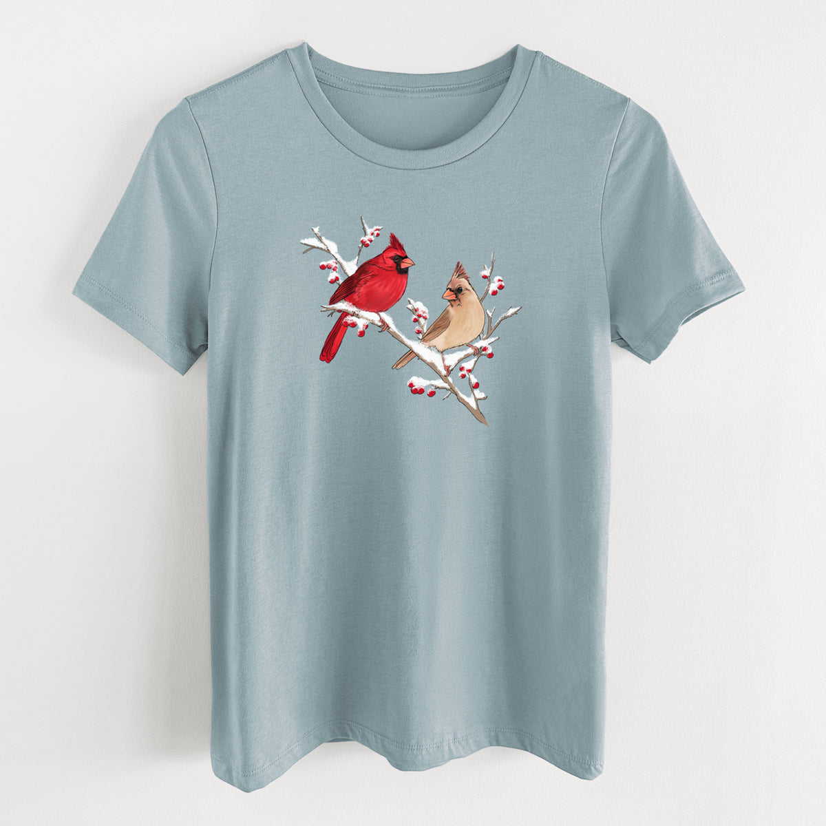 Vintage denim women's relaxed fit cotton t-shirt laid flat, printed with a full-color illustration of a male and female northern cardinal perched on a snowy branch with red berries.