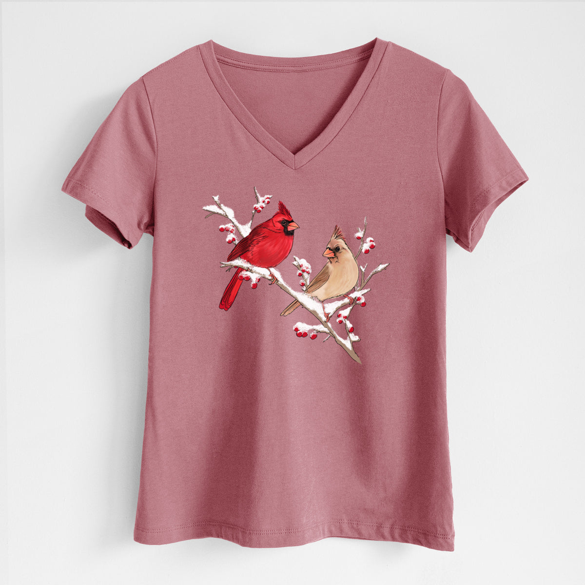 Mauve pink women's relaxed fit cotton V-neck t-shirt laid flat, printed with a full-color illustration of a male and female northern cardinal perched on a snowy branch with red berries.