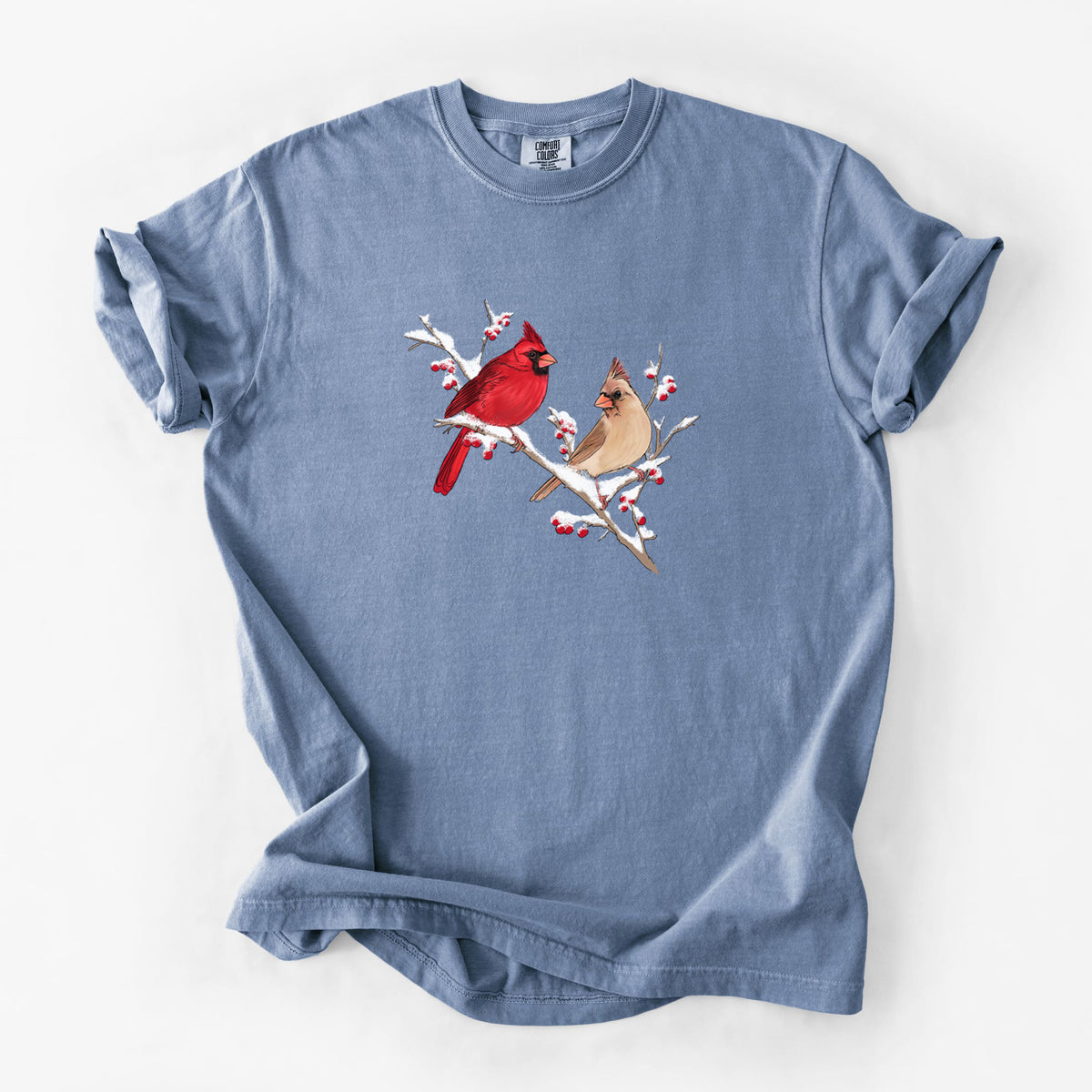 Blue jean Comfort Colors t-shirt laid flat, printed with a full-color illustration of a male and female northern cardinal perched on a snowy branch with red berries.