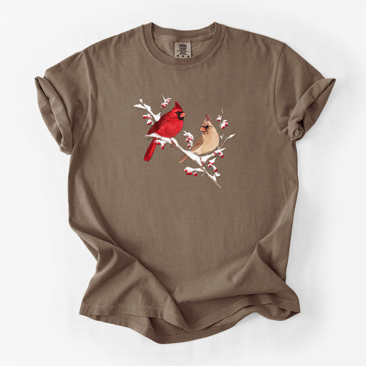 Espresso brown Comfort Colors t-shirt laid flat, printed with a full-color illustration of a male and female northern cardinal perched on a snowy branch with red berries.