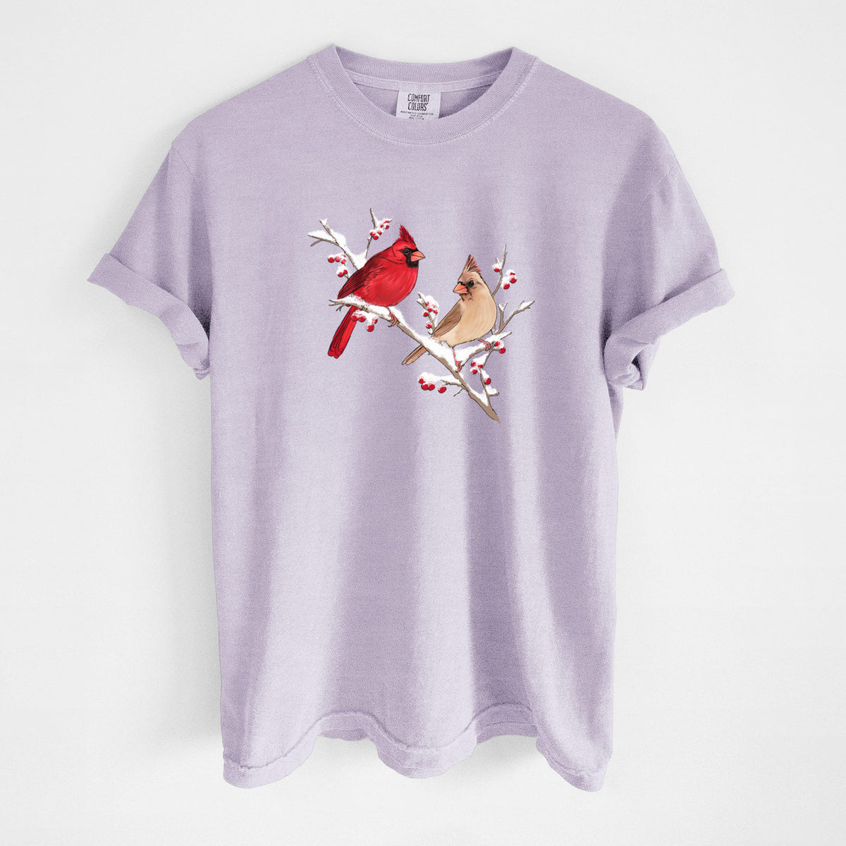 Orchid purple Comfort Colors t-shirt laid flat, printed with a full-color illustration of a male and female northern cardinal perched on a snowy branch with red berries.