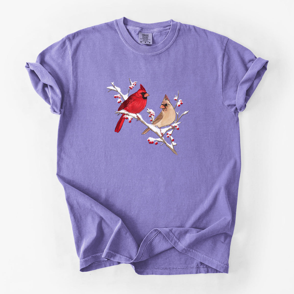 Violet purple Comfort Colors t-shirt laid flat, printed with a full-color illustration of a male and female northern cardinal perched on a snowy branch with red berries.