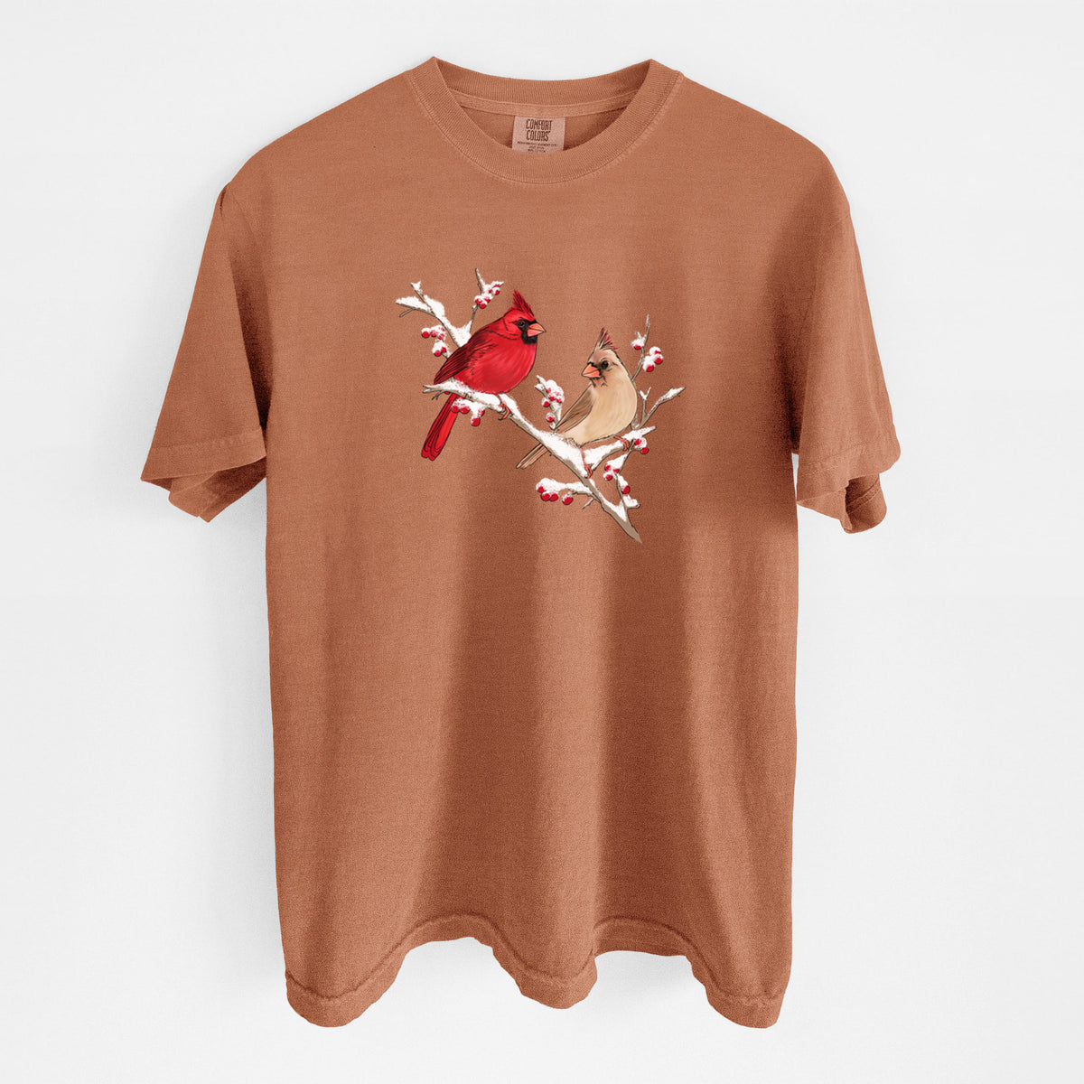 Yam burnt orange Comfort Colors t-shirt laid flat, printed with a full-color illustration of a male and female northern cardinal perched on a snowy branch with red berries.