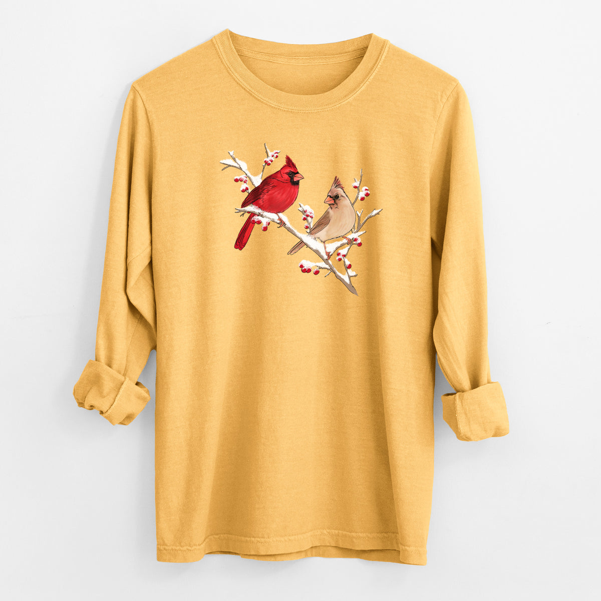 Golden wheat yellow Comfort Colors long sleeve shirt laid flat with the cuffs rolled, printed with a full-color illustration of a male and female northern cardinal perched on a snowy branch with red berries.